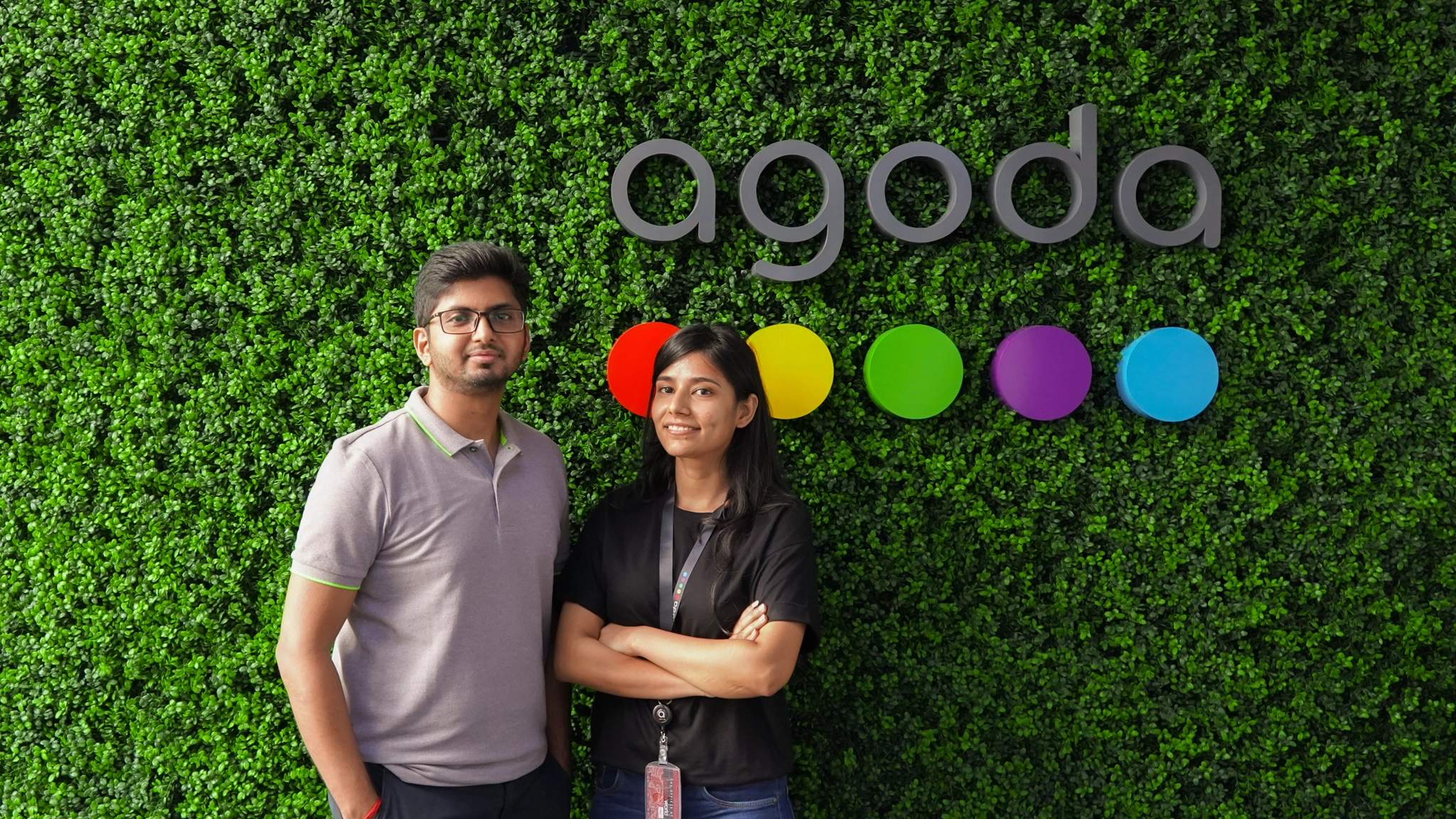 Amitansh & Anjali - Full Stack engineers at Agoda in front of the Agoda logo in the Bangkok office